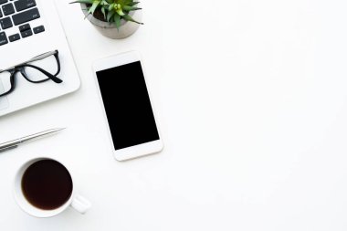 Beyaz akıllı telefon beyaz ekranlı en üst beyaz ofis masasında dizüstü bilgisayar, kahve ve malzeme ile birlikte. Kopyalama alanı olan üst görünüm, düz yatay.