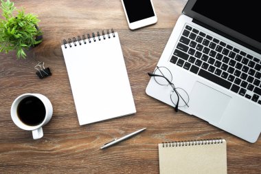 Boş defter sayfası ahşap ofis masasının üstünde dizüstü bilgisayar, kahve ve malzeme ile birlikte. Kopyalama alanı olan üst görünüm, düz yatay.