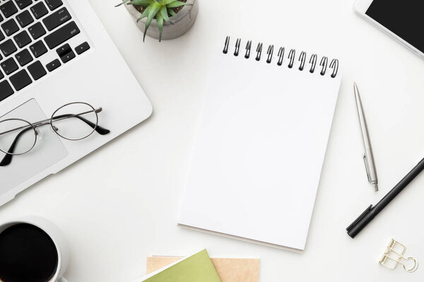 White office desk table with blank notebook and supplies. Top view, flatl lay.