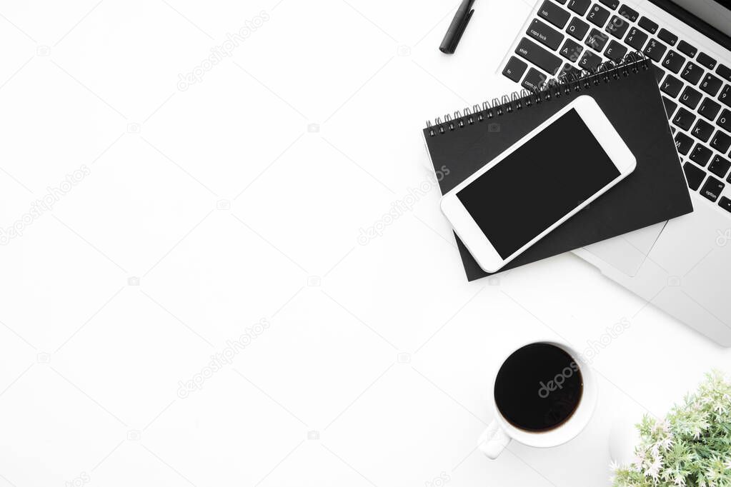 White office desk table with smartphone with blank mock up screen, laptop computer, cup of coffee and supplies. Top view with copy space, flat lay.