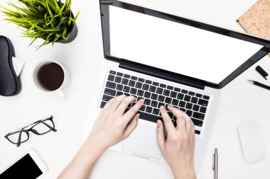 Boş dizüstü bilgisayar ekranı, elleri klavyede beyaz ofis masasının üzerinde malzemelerle yazı yazıyor. Üst manzara, düz uzanma.