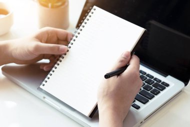 Modern ofiste dizüstü bilgisayarın üzerinde boş defter ve kalem tutan eller..