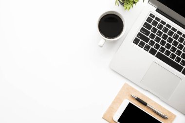 Laptop bilgisayarı, akıllı telefon, kahve ve malzemelerle dolu beyaz ofis masası. Kopyalama alanı olan üst görünüm, düz yatay.