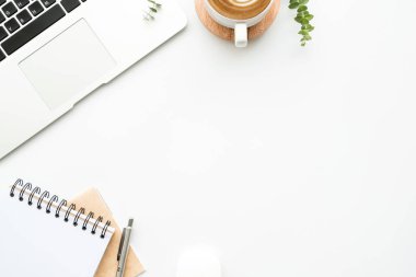 Laptop bilgisayarlı beyaz minimalist ofis masası, bir fincan kahve, kalem ve malzemelerle dolu defterler. Kopyalama alanı olan üst görünüm, düz görünüm, en düşük biçim.
