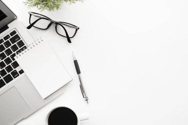 Boş defterli beyaz ofis masası. Kalem, dizüstü bilgisayar, kahve ve malzemeler. Kopyalama alanı olan üst görünüm, düz yatay.