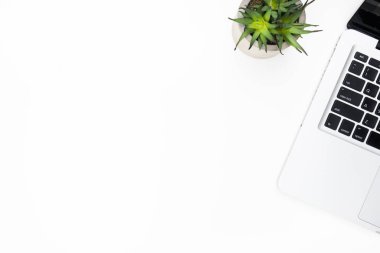 Laptop bilgisayarı ve kaktüs tenceresi olan beyaz, minimal ofis masası. Fotokopi alanı olan üst görünüm, düz. Hipster masaüstü konsepti.