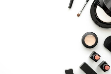 Güzellik kozmetiklerinin bembeyaz arka planda ruj, kapatıcı, temel pudrası ve fırçayla yapılmış düz bir resmi vardı. Metnin için kopyalama alanı olan en üstteki görünüm.