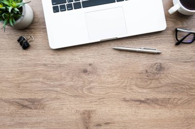 Dizüstü bilgisayarlı ahşap ofis masası, bir fincan kahve ve malzeme. Kopyalama alanı olan üst görünüm, düz yatay.