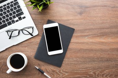 Beyaz akıllı telefonlu ahşap masa masası. Ekran, dizüstü bilgisayar, kahve ve malzemeler. Kopyalama alanı olan üst görünüm, düz yatay.