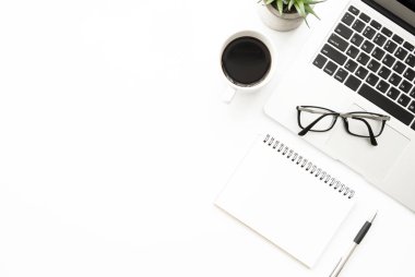 Boş defterli beyaz ofis masası. Kalem, dizüstü bilgisayar, kahve ve malzemeler. Kopyalama alanı olan üst görünüm, düz yatay.