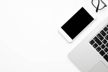 Beyaz akıllı telefon beyaz ofis masasının üstünde dizüstü bilgisayarla birlikte. Kopyalama alanı olan üst görünüm, düz yatay.