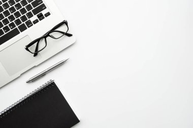 Dizüstü bilgisayarlı beyaz minimalist ofis masası kalem ve gözlüklü defter. Kopyalama alanı olan en üst görünüm, düz uzanma biçimi en aza indir.