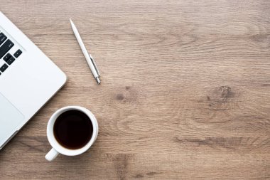 Dizüstü bilgisayarlı ahşap ofis masası, bir fincan kahve ve kalem. Kopyalama alanı olan üst görünüm, düz yatay.