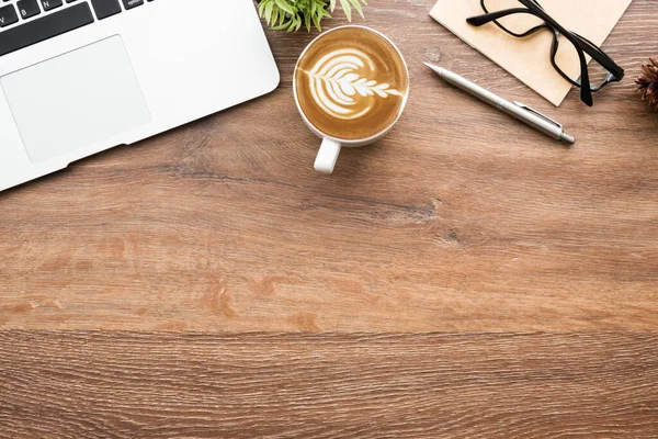 Wood minimalist office desk table with laptop computer, cup of cafe lattee coffee and office supplies. Top view with copy space, flat lay, minimal style.