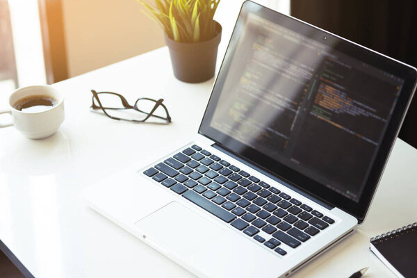 Wood programmer office desk table with laptop with the software code displaying on it.