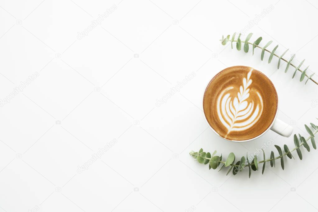 Cup of cafe latte coffee is on top of white table with branches of eucalyptus. Top view with copy space, flat lay.