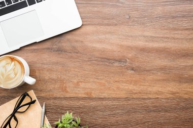 Diz üstü bilgisayarlı ahşap ofis masası, bir fincan kahve ve malzeme. Kopyalama alanı olan üst görünüm, düz yatay.