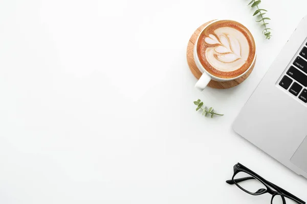 White minimalist office desk table with laptop computer, cup of latte cofee and supplies. Top view with copy space, flat lay, minimal style.