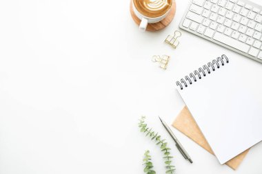 Boş defter, bir fincan kahve ve ofis malzemeleri olan beyaz, minimal ofis masası. Kopyalama alanı olan üst görünüm, düz yatay.