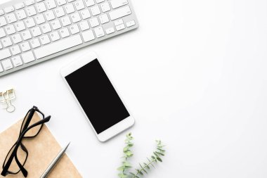 Beyaz ekranlı akıllı telefon beyaz ofis masasının üstünde malzemelerle birlikte. Kopyalama alanı olan üst görünüm, düz yatay.