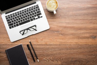 Dizüstü bilgisayarı, kahve ve malzemeleri olan ahşap minimum hippi ofis masası. Kopyalama alanı olan üst görünüm, düz yatay.