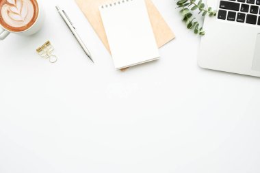 Laptop bilgisayarı, kahve ve malzemelerle dolu beyaz minimalist ofis masası. Kopyalama alanı olan üst görünüm, düz yatay.