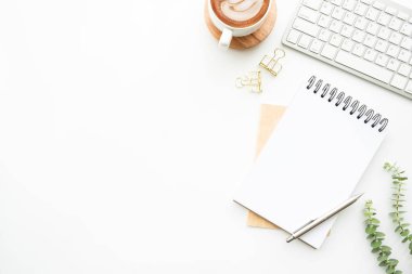 Boş defter, kahve ve malzemelerle dolu, en az beyaz ofis masasının üstünde. Kopyalama alanı olan üst görünüm, düz yatay.