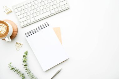 Boş defter, kahve ve malzemelerle dolu, en az beyaz ofis masasının üstünde. Kopyalama alanı olan üst görünüm, düz yatay.