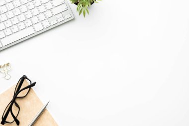 Bilgisayar klavyesi ve malzemeleri olan beyaz ofis masası. Kopyalama alanı olan üst görünüm, düz yatay.
