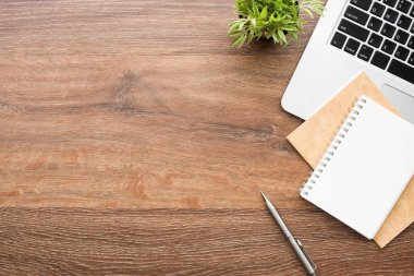 Ahşap ofis masasında boş defter, kalem, dizüstü bilgisayar ve malzemeler. Kopyalama alanı olan üst görünüm, düz yatay.