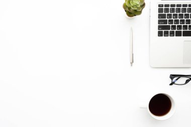 Laptop bilgisayarı, kahve ve malzemelerle dolu beyaz, minimal ofis masası. Kopyalama alanı olan üst görünüm, düz yatay.