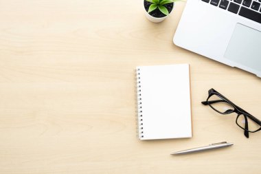 Ahşap ofis masası boş defter sayfası, kalem, dizüstü bilgisayar ve malzemeler. Kopyalama alanı olan üst görünüm, düz yatay.