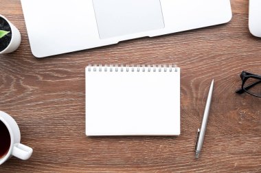 Boş defter sayfası ahşap ofis masasının üstünde bir sürü şey var. Üst manzara, düz uzanma.
