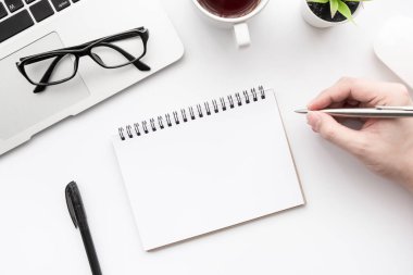 Erkek eli boş bir defter sayfasına beyaz ofis masasının üzerine bir şeyler yazacak. Kopyalama alanı olan üst görünüm, düz yatay.