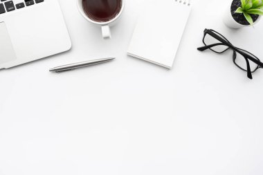 Laptop bilgisayarlı beyaz ofis masası, boş defter sayfası, kahve ve malzemeler. Kopyalama alanı olan üst görünüm, düz yatay.