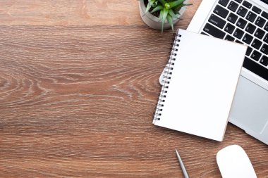 Ahşap ofis masası dizüstü bilgisayarlı, kalemli ve malzemeli boş defter. Kopyalama alanı olan üst görünüm, düz yatay.