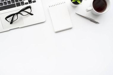 Küçük boş defterli beyaz ofis masası, dizüstü bilgisayar kahve ve ofis malzemeleri. Kopyalama alanı olan üst görünüm, düz yatay.
