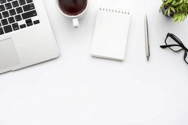 Küçük boş defterli beyaz ofis masası, dizüstü bilgisayar kahve ve ofis malzemeleri. Kopyalama alanı olan üst görünüm, düz yatay.