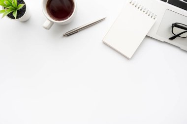 Küçük boş defterli beyaz ofis masası, dizüstü bilgisayar kahve ve ofis malzemeleri. Kopyalama alanı olan üst görünüm, düz yatay.