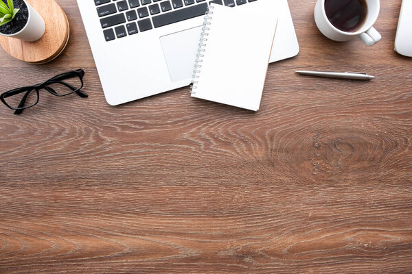 Деревянный стол с чистым блокнотом, ноутбуком и принадлежностями. Вид сверху с копировальным пространством, плоская кладка.