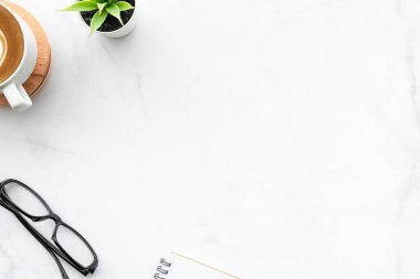Minimum beyaz mermer ofis masası, bir fincan kahve, defter ve malzemeler. Kopyalama alanı olan üst görünüm, düz yatay.