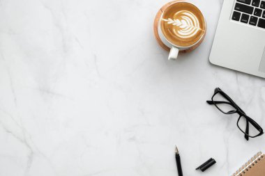 Laptop bilgisayarlı beyaz mermer ofis masası, bir fincan kahve ve ofis malzemeleri. Kopyalama alanı olan üst görünüm, düz yatay.