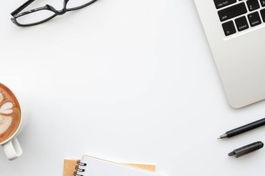 Laptop bilgisayarlı beyaz ofis masası, bir fincan kahve ve malzemeler. Kopyalama alanı olan üst görünüm, düz yatay.