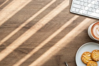 Bilgisayarlı ahşap ofis masası, bir fincan kahve ve bir tabak bademli kurabiye. Fotokopi alanı olan üst görünüm, düz. Sabah konseptinde ofis hayatı.