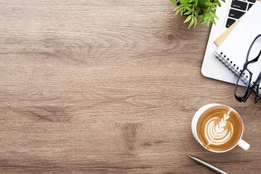 Diz üstü bilgisayarlı ahşap ofis masası, bir fincan kahve ve ofis malzemeleri. Kopyalama alanı olan üst görünüm, düz yatay.