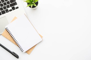 Boş defter, kalem ve dizüstü bilgisayarlı beyaz ofis masası. Kopyalama alanı olan üst görünüm, düz yatay.
