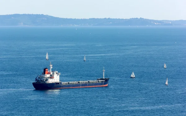 Cargo Ship Surrounded by Sailboats — Stock Photo, Image