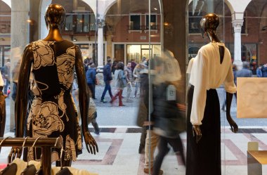 PADUA, İtalya - 21 Şubat 2016: Kadın elbiseleri giyen iki manken şık bir giyim mağazasının vitrininde kalabalık bir şehir merkezine bakıyor