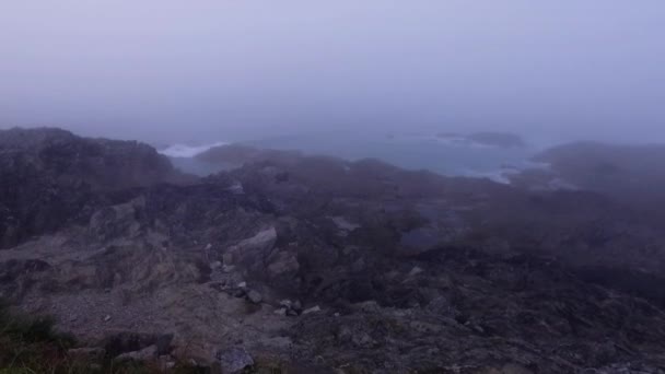 Costa brumosa, olas, movimiento pan alrededor para revelar surfistas en trajes de neopreno caminando con tablas a lo largo de un camino costero . — Vídeo de stock