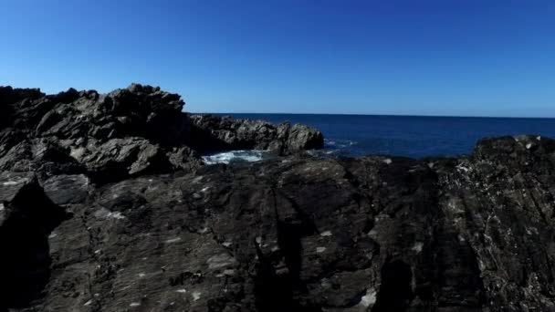 Gentle upward motion pan over coastal rock to reveal horizon of blue sea and sky. — Stock Video
